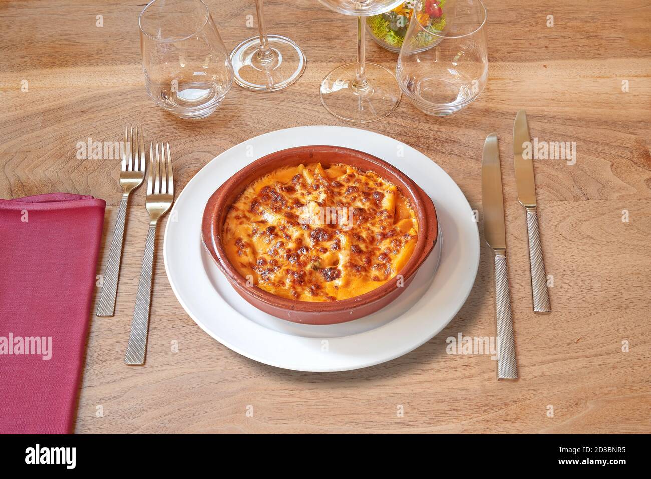 Argenteria su tavolo di legno marrone e gratin bianco di maccheroni in ciotola di ceramica. Foto Stock