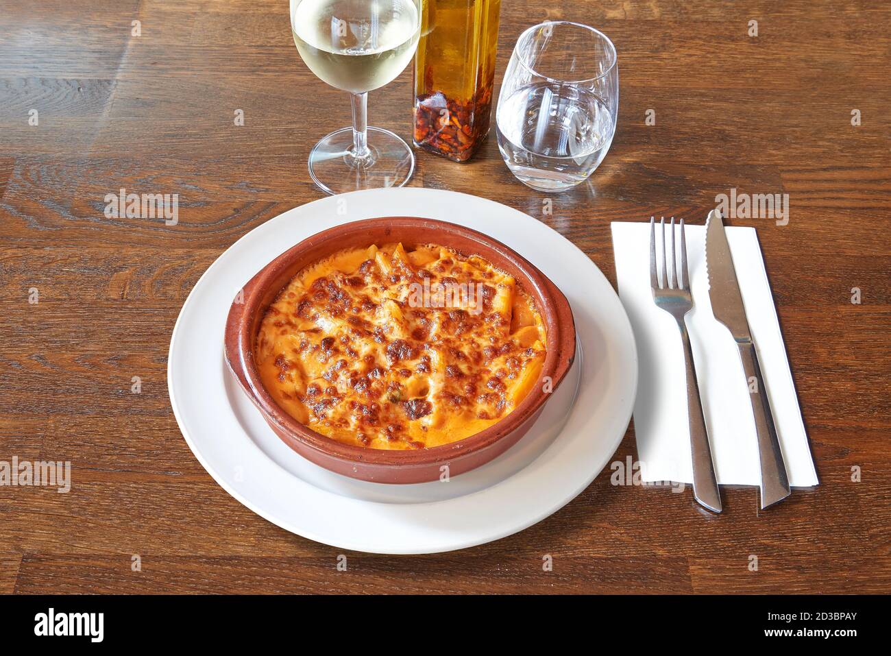 Argenteria su tavolo di legno marrone e gratin bianco di maccheroni in ciotola di ceramica. Foto Stock