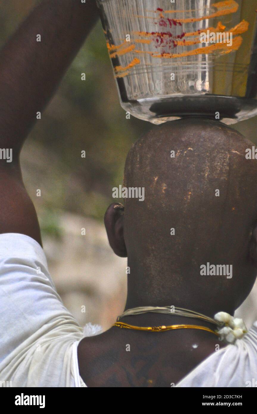 Vista posteriore della testa rasata di un giovane devoto indù che porta un'urna di latte come offerta durante le celebrazioni del Thaipusam. Foto Stock