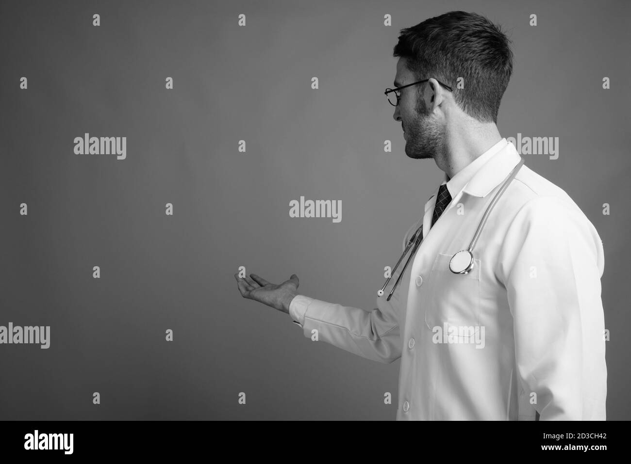 Giovane bel medico uomo che indossa occhiali su sfondo grigio Foto Stock
