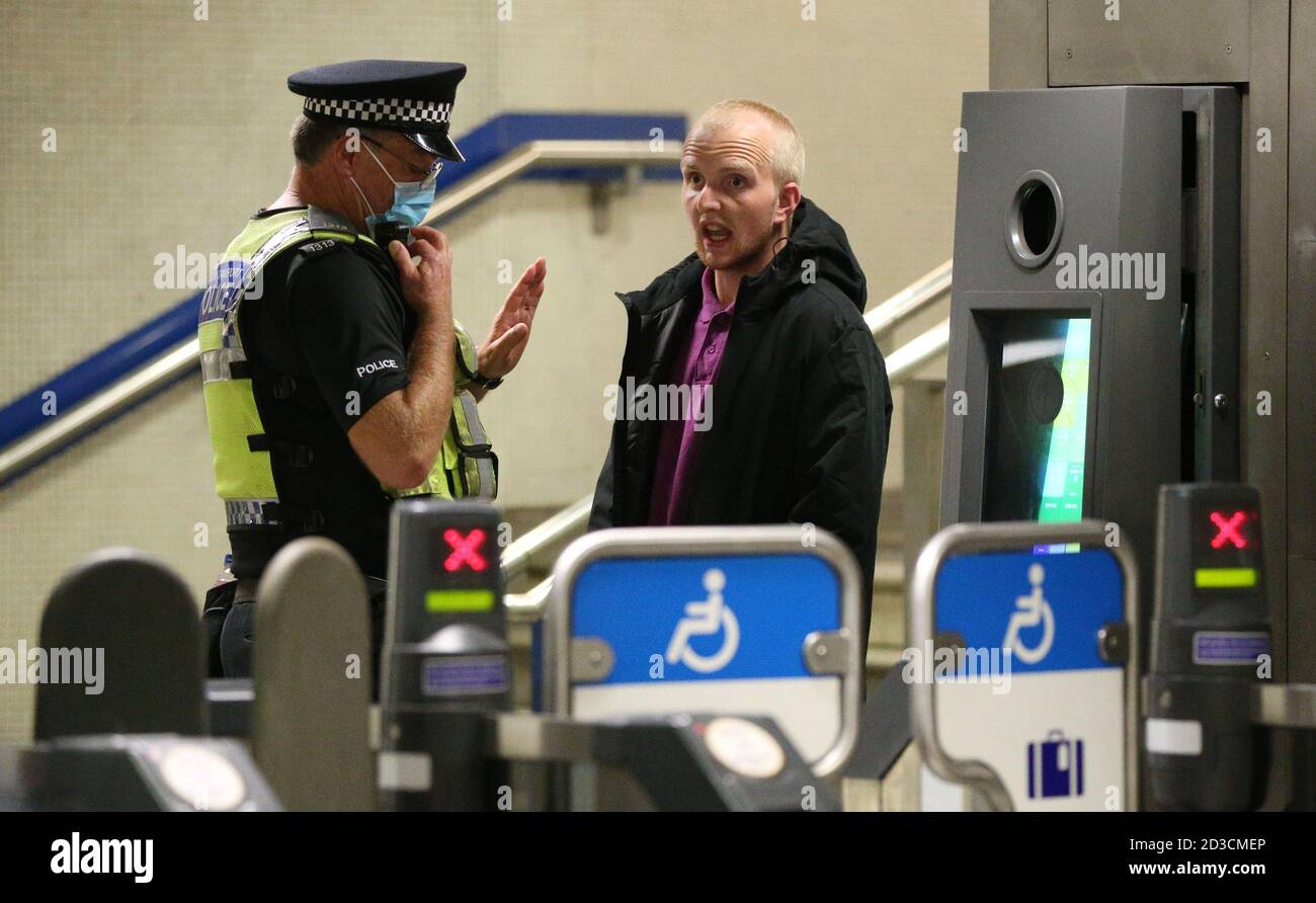 Un uomo reagisce ad essere avvertito da un ufficiale britannico della polizia di trasporto per non indossare una maschera facciale alla stazione della metropolitana di King's Cross, Londra. Foto Stock