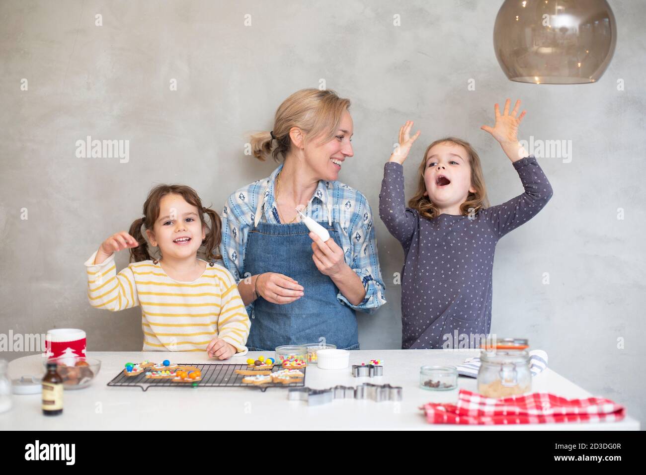 Donna bionda che indossa grembiule blu e due ragazze che cottura biscotti di Natale. Foto Stock