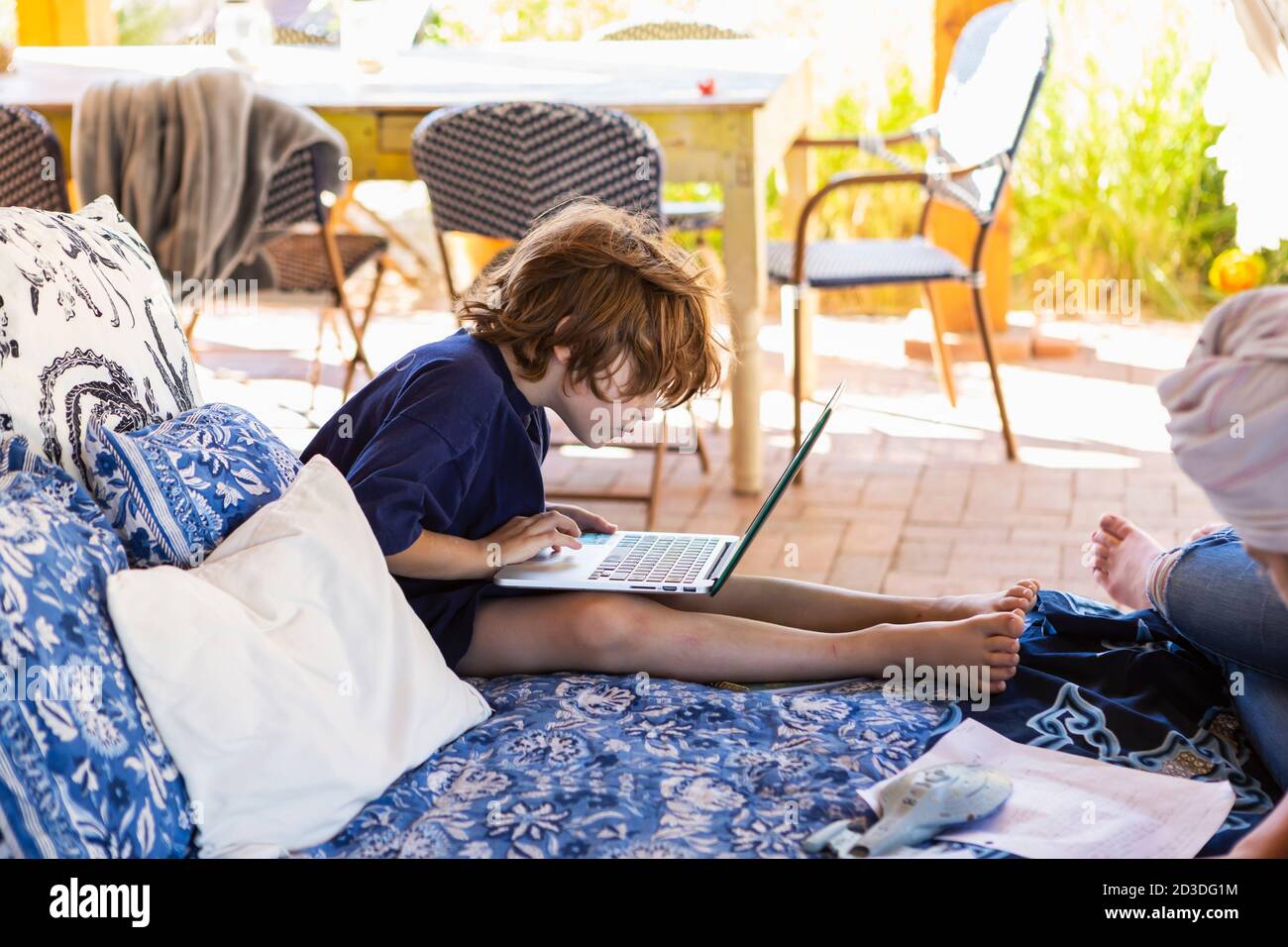 Ragazzo con i capelli marroni seduti sul letto esterno, facendo i compiti sul computer portatile. Foto Stock