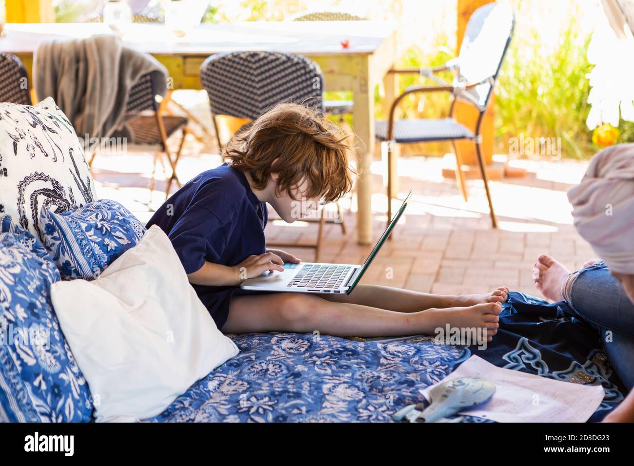 Ragazzo con i capelli marroni seduti sul letto esterno, facendo i compiti sul computer portatile. Foto Stock