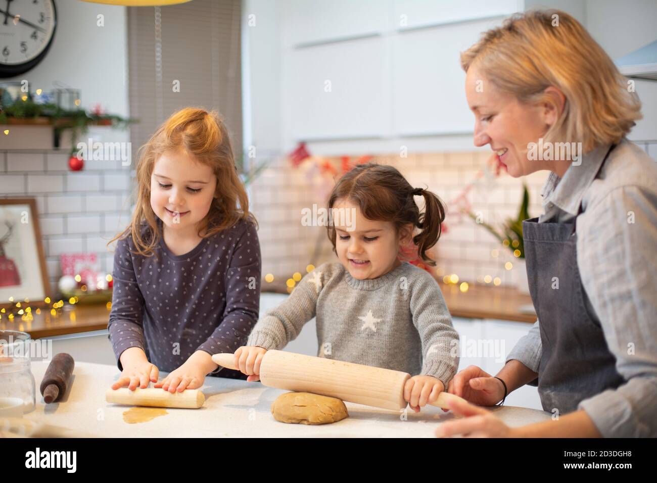 Donna bionda che indossa grembiule blu e due ragazze in piedi in cucina, cucinando i biscotti di Natale. Foto Stock