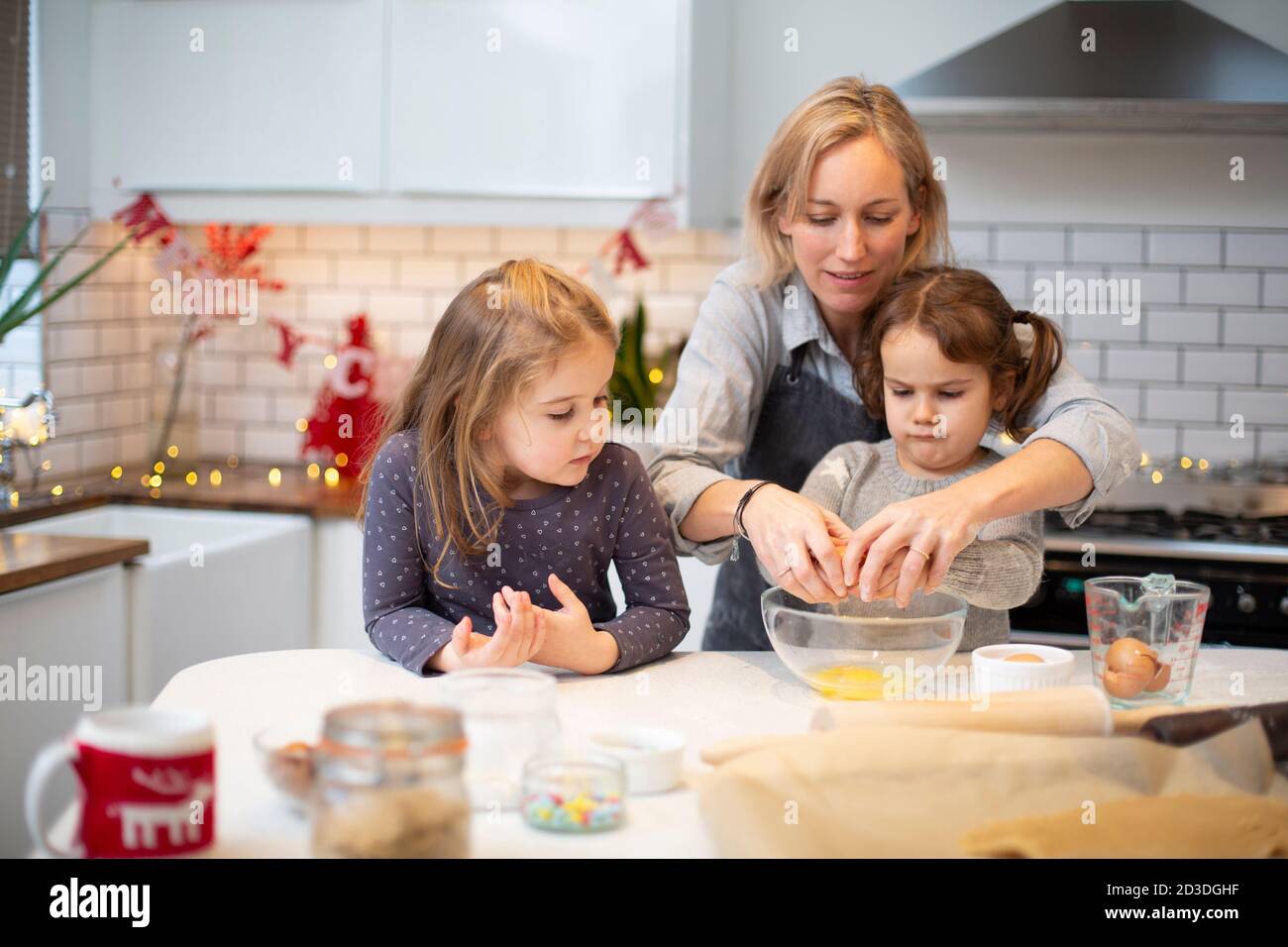 Donna bionda che indossa grembiule blu e due ragazze in piedi in cucina, cucinando i biscotti di Natale. Foto Stock