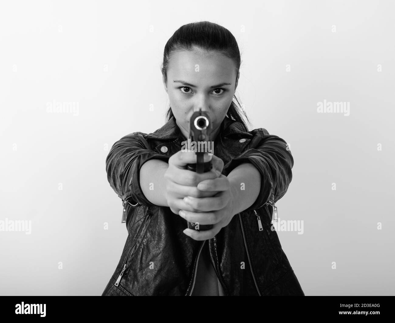 Primo piano della giovane donna asiatica che punta la pistola alla macchina fotografica con entrambe le mani su sfondo bianco Foto Stock
