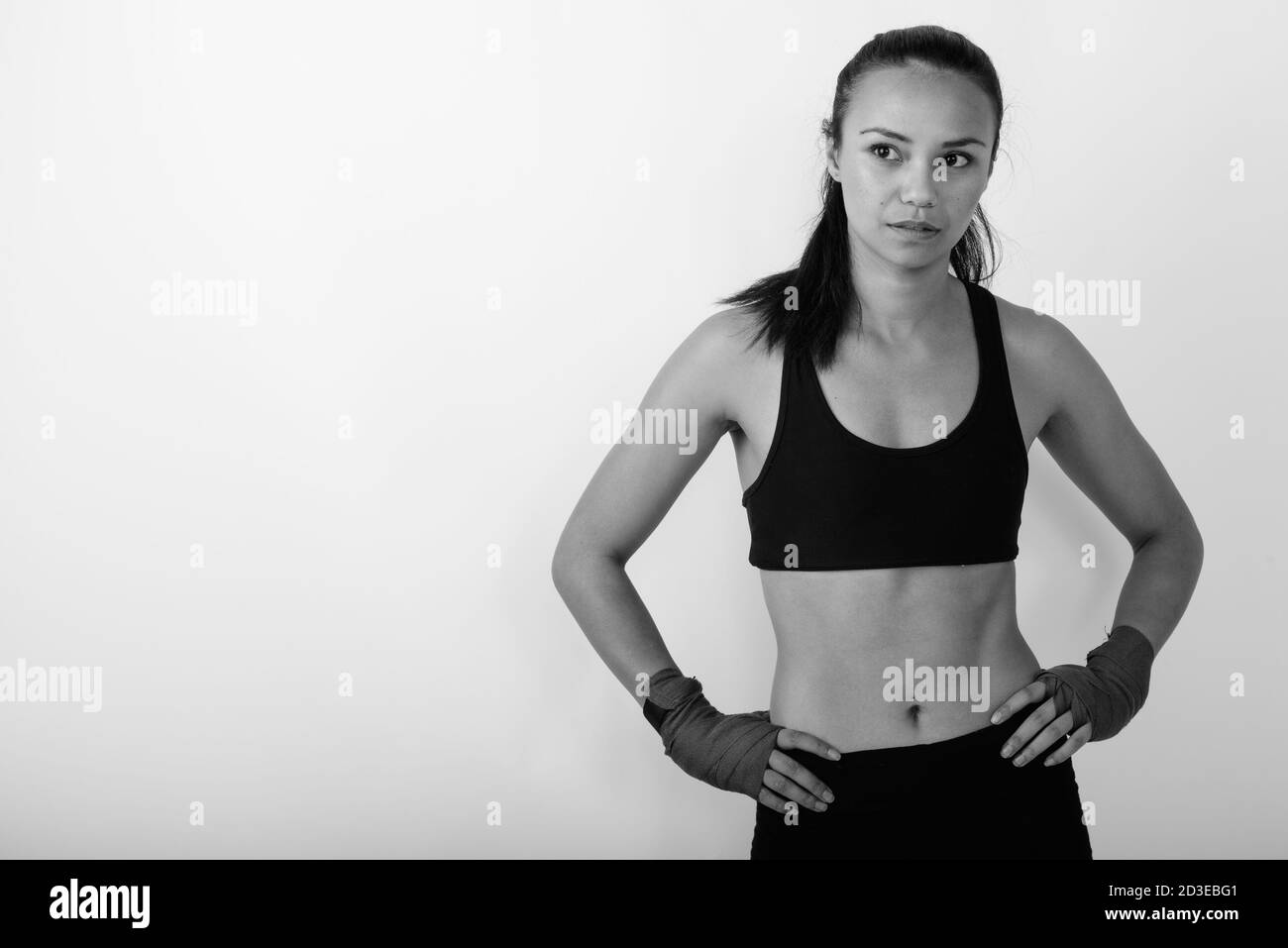 Studio girato di giovane donna asiatica combattente pensare mentre posa con le mani sui fianchi su sfondo bianco Foto Stock