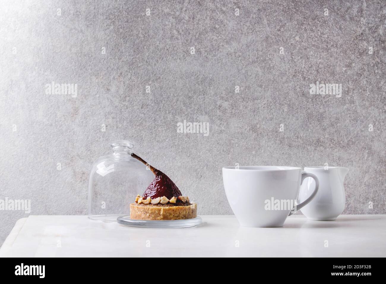 Vino rosso dolce pera tartlet con tazza di caffè espresso e la brocca di crema piedi su marmo bianco tavola con muro grigio a sfondo. Stile minimalista Foto Stock