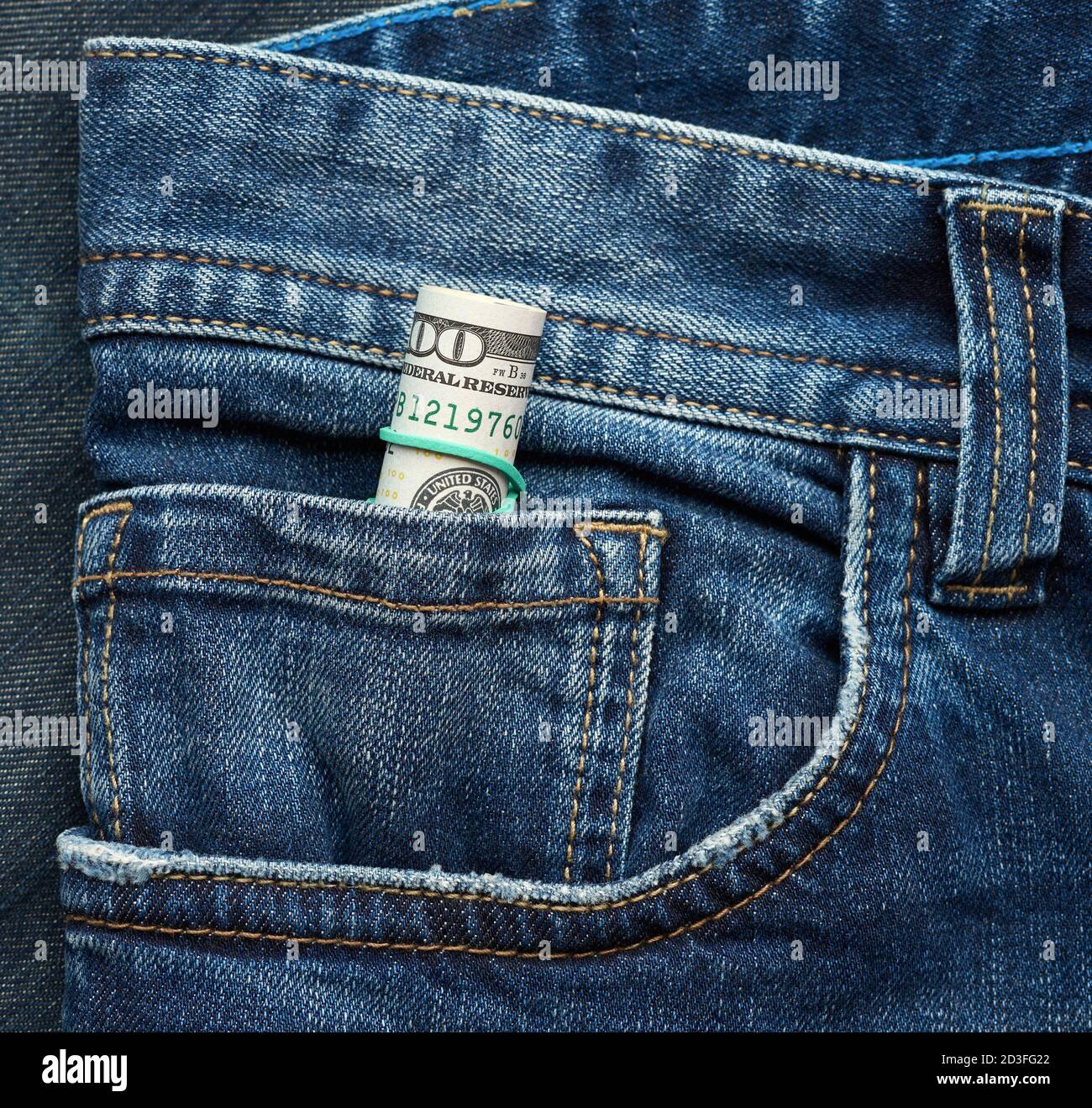 arrotolato carta cento dollari fatture e stretto con banda di gomma verde su sfondo blu denim, primo piano Foto Stock