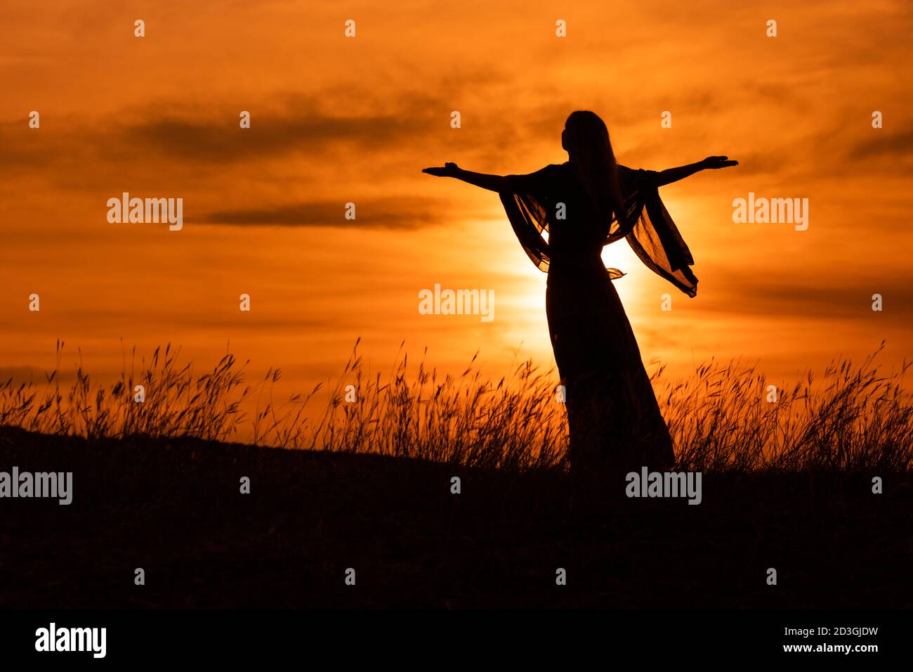 Silhouette di una donna con le braccia allungate che guarda il tramonto bello. Foto Stock