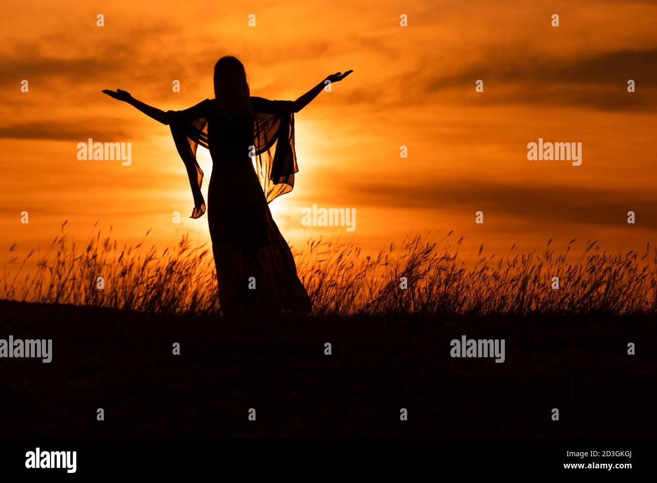 Silhouette di una donna con le braccia allungate che guarda il tramonto bello. Foto Stock