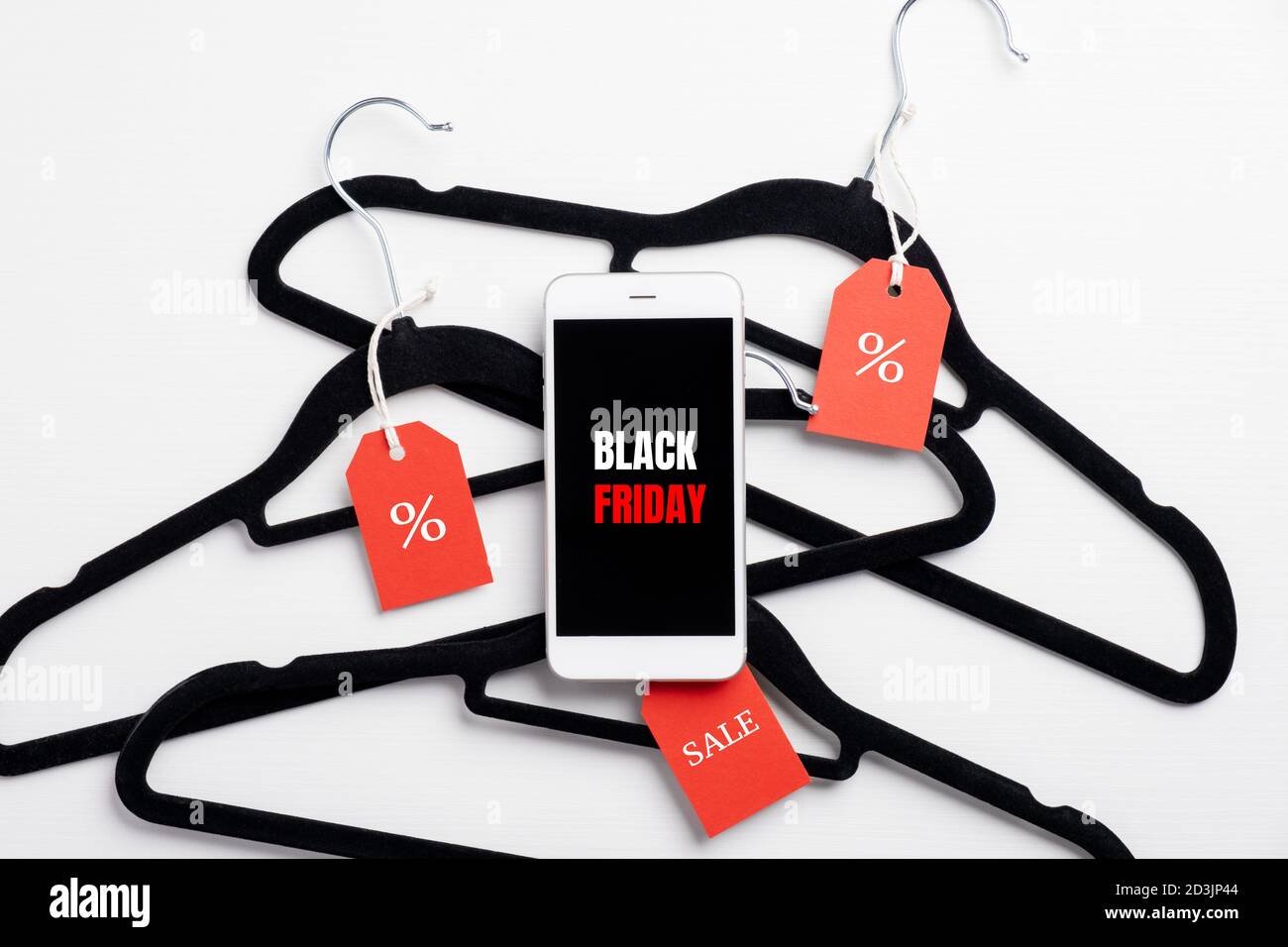 Vendita del Black Friday. Appendiabiti con etichette e telefono cellulare con il segno 'Black Friday' sullo schermo su sfondo bianco. Disposizione piatta, vista dall'alto. Foto Stock