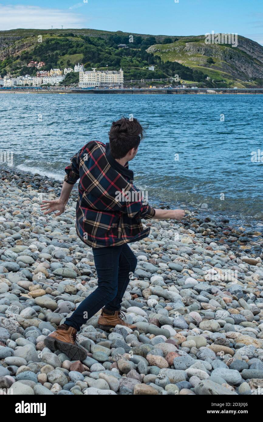Uomo gettando ciottoli nel mare a Llandudno North Shore spiaggia Foto Stock