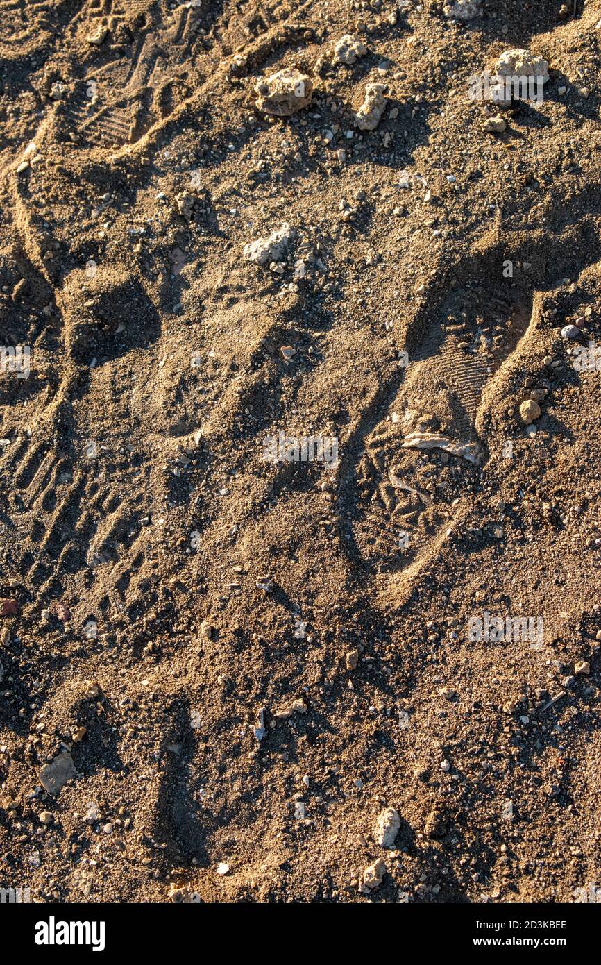 Consistenza di sabbia e pietre in cui sono un'impronta di scarpe della gente con ombre dure. Foto Stock