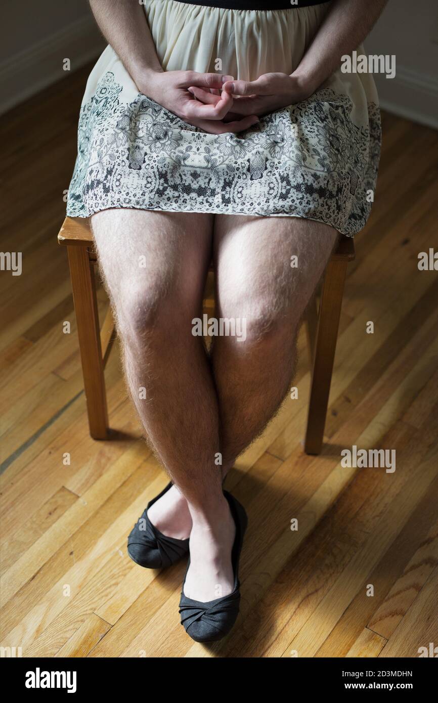 Mani piegate in grembo di persona seduta indossando una gonna con caratteristiche maschili. Foto Stock