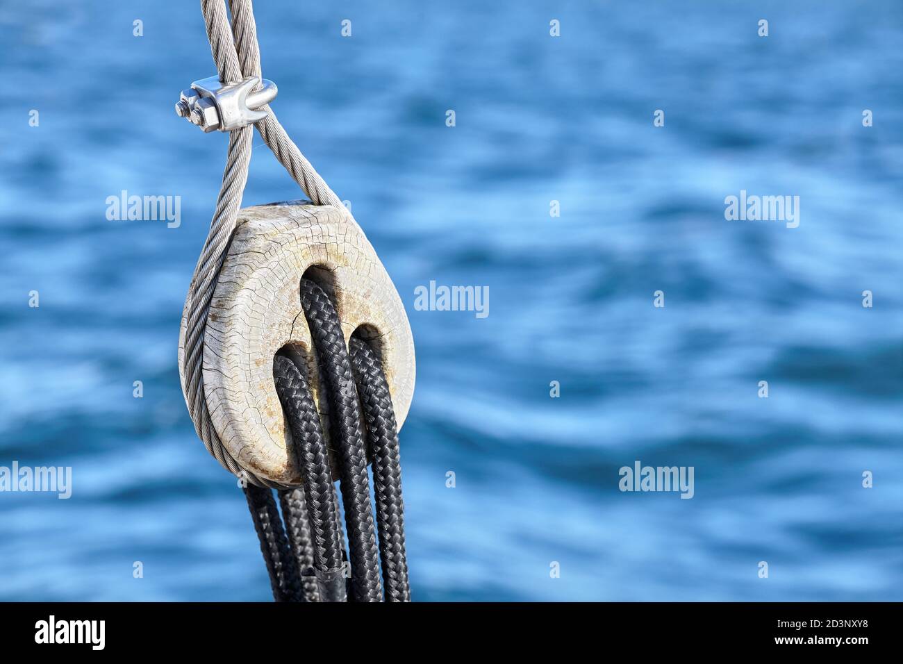 Vecchio blocco di puleggia di legno con mare blu sullo sfondo, fuoco selettivo. Foto Stock