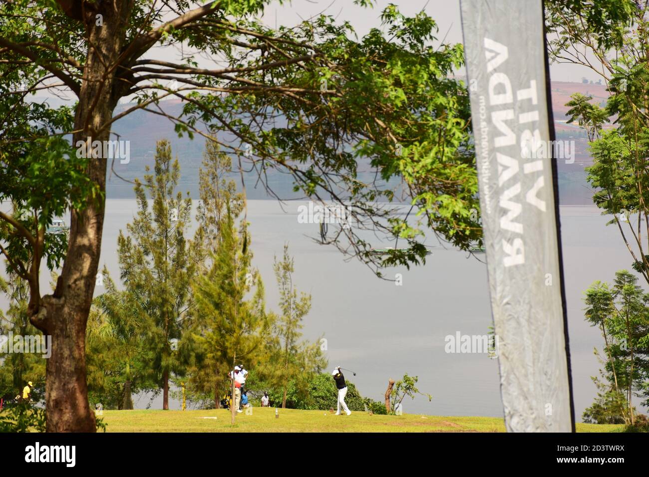La gente gioca a golf in un campo vicino al lago Muhazi, con il banner di goccia Ruanda Visit e gli alberi nella foto Foto Stock