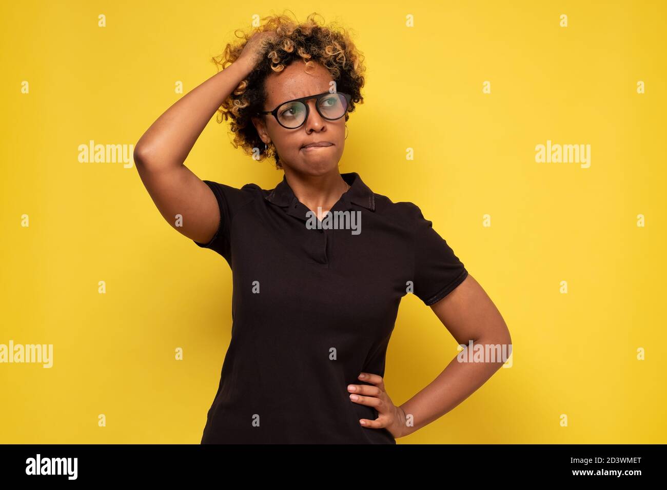 Giovane donna africana in occhiali graffiando la testa, pensando daysognando profondamente qualcosa Foto Stock