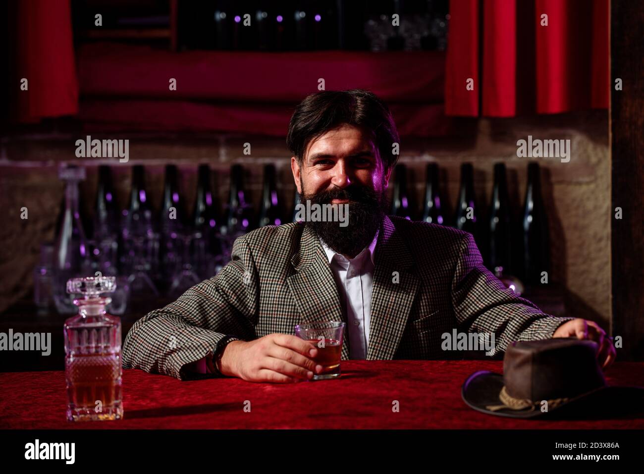 Uomo lavoratore vintage con barba lunga che tiene il whiskey. Seduto al bar. Foto Stock