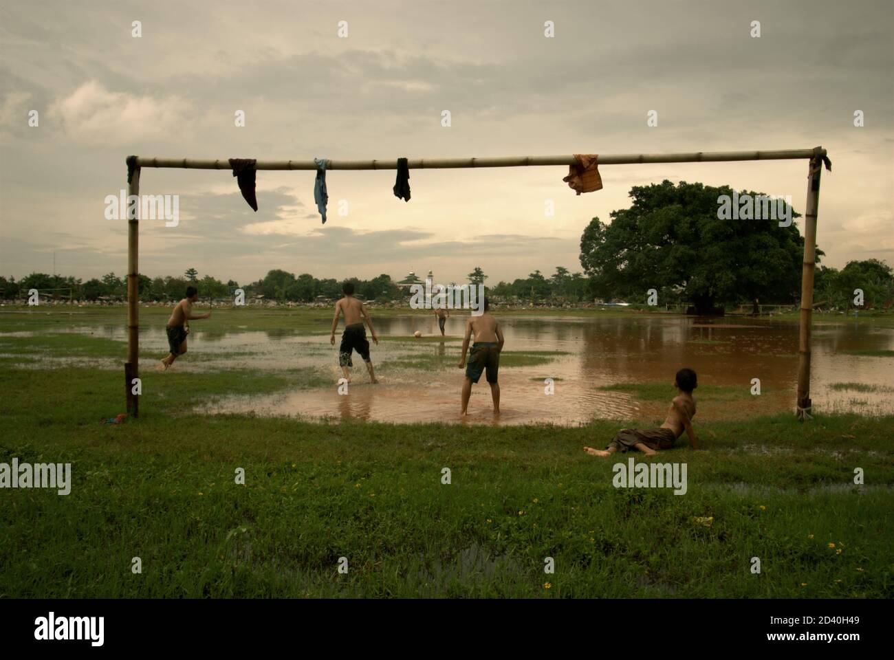 I bambini giocano a calcio su un campo, parzialmente allagato e situato tra due cimiteri pubblici a Pondok Kelapa, Giacarta, Indonesia. Foto Stock