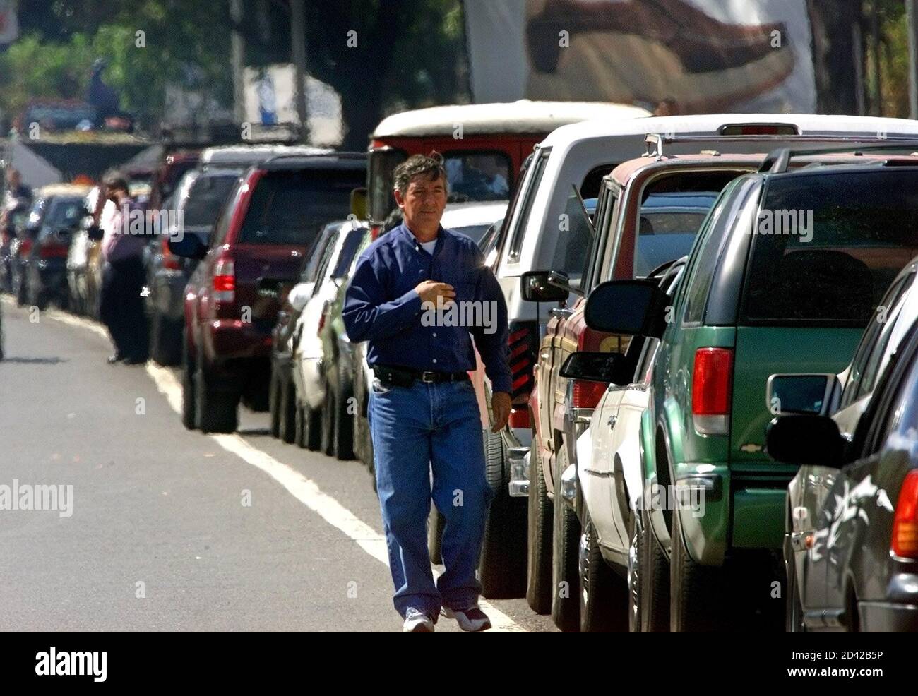 Un uomo cammina attraverso una enorme linea di auto in attesa di acquistare benzina a Caracas, Venezuela, 26 dicembre 2002. I venezuelani continuano a subire carenze di benzina nella quarta settimana di uno sciopero contro il presidente Hugo Chavez che ha ridotto la produzione di petrolio e ridotto le esportazioni da parte`s esportatore mondiale di petrolio n.5. REUTERS/Jorge Silva JS/HB Foto Stock