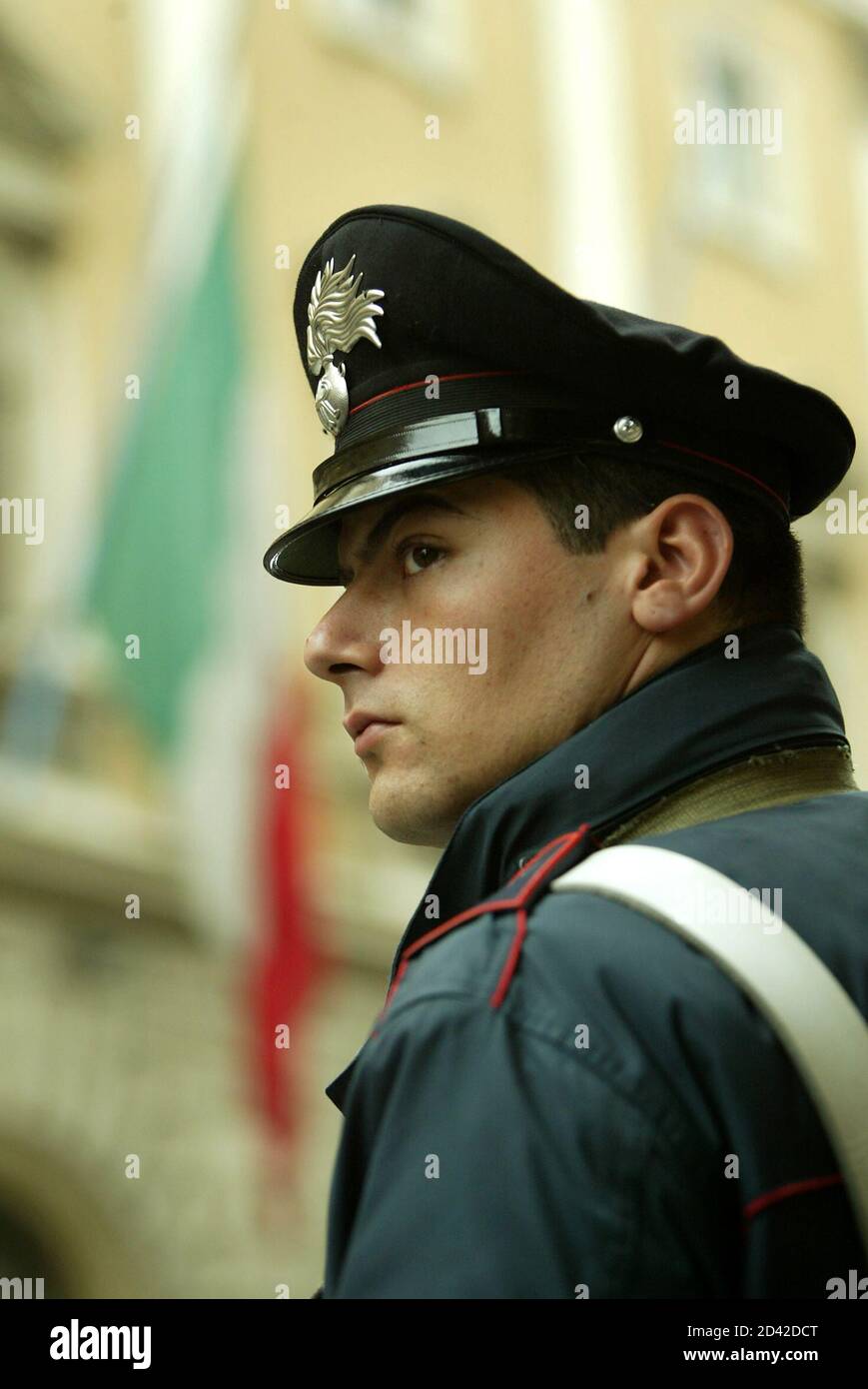 Un carabiniere sorge guardia come una bandiera italiana vola a mezzo albero fuori dal Ministero della Difesa nel centro di Roma 12 novembre 2003. Una bomba ha strappato attraverso una base militare italiana di polizia mercoledì nella città irachena di Nassiriya, uccidendo almeno 14 italiani e otto iracheni. REUTERS/Alessandro Bianchi PP03110055 DJM Foto Stock