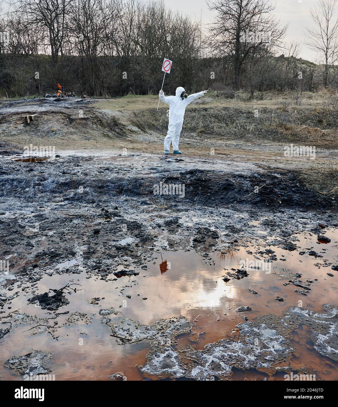 Ricercatore in tuta protettiva bianca e maschera a gas che installa un cartello di avvertenza, nessun cartello d'ingresso, sul territorio contaminato. Acqua fangosa sporca arrugginita per analisi. Concetto di disastro ecologico Foto Stock
