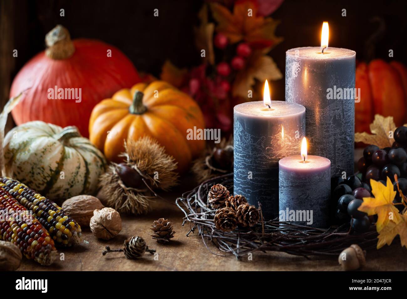 Concetto di vendemmia autunnale o autunnale con candele accese, zucche decorative, mais, noci, uva e pineconi Foto Stock