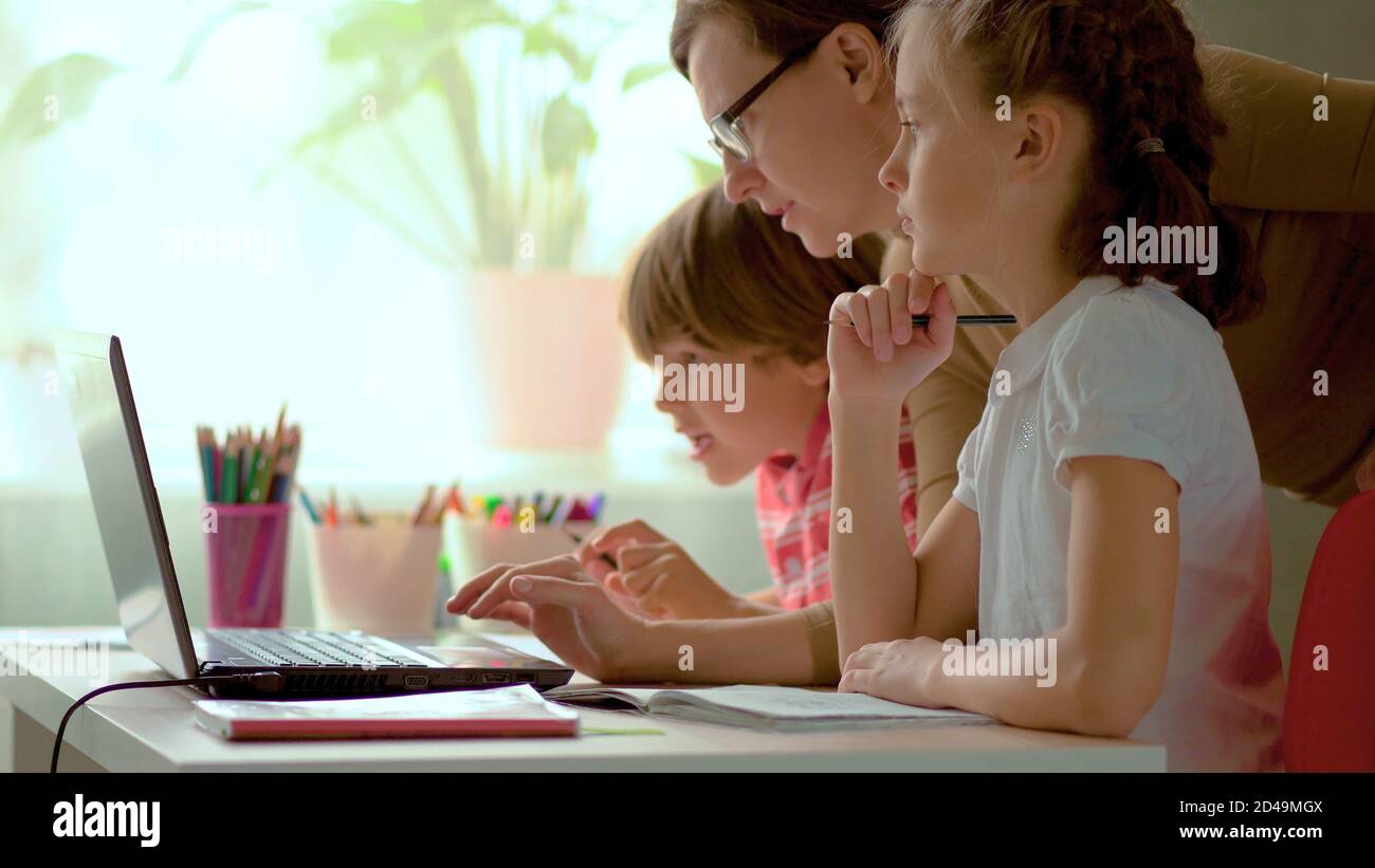 I bambini carini usano il laptop per l'istruzione, lo studio in linea, lo studio domestico, il ragazzo e la ragazza hanno compiti a distanza imparando. Concetto di stile di vita per la scuola domestica. Madre aiuta figlia e figlio. Foto Stock