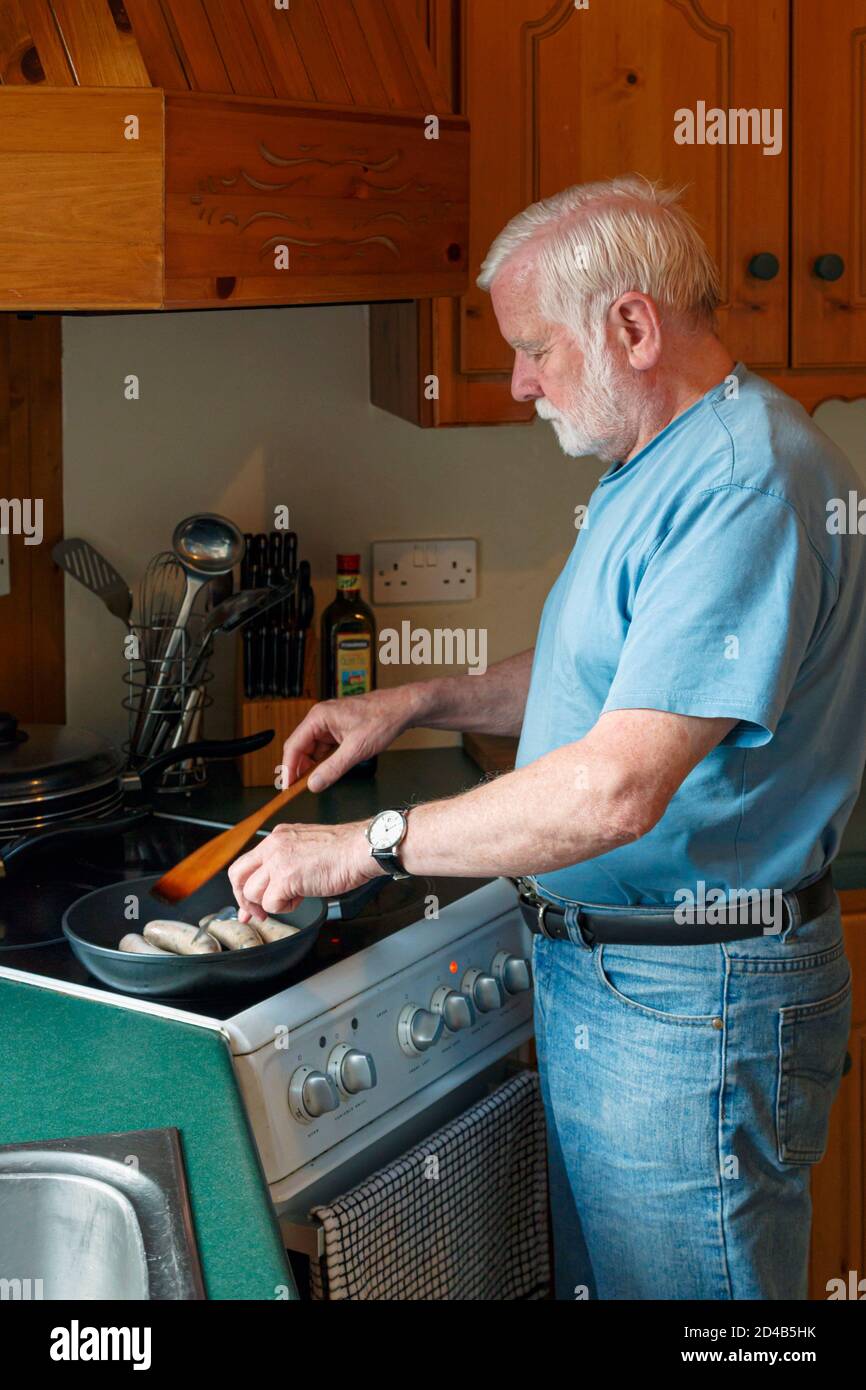 Uomo anziano che cucinano salsicce in cucina. Foto Stock
