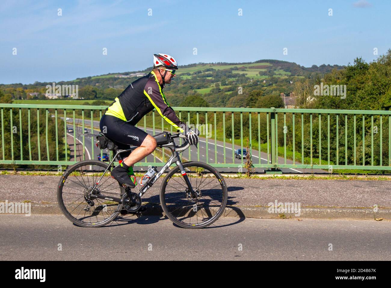 Ciclista maschile equitazione Ridley sport bici da strada sulla strada di campagna che attraversa il ponte autostradale nella rurale Lancashire, Regno Unito Foto Stock