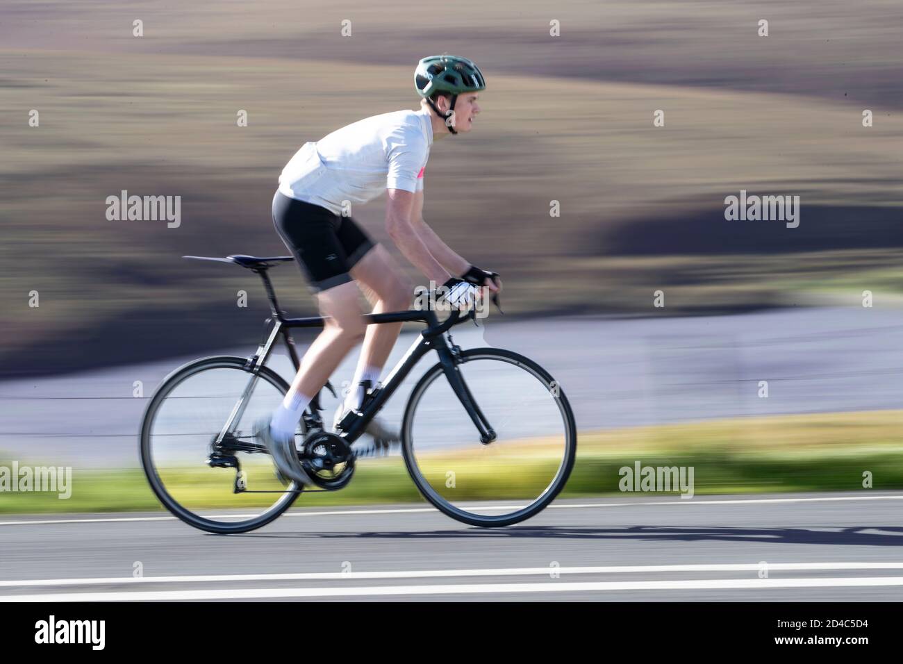 Un giovane ciclista che corre a velocità elevata fuori dalla sella Una strada in salita sulle Yorkshire Moors con sfocatura del movimento sfondo Foto Stock