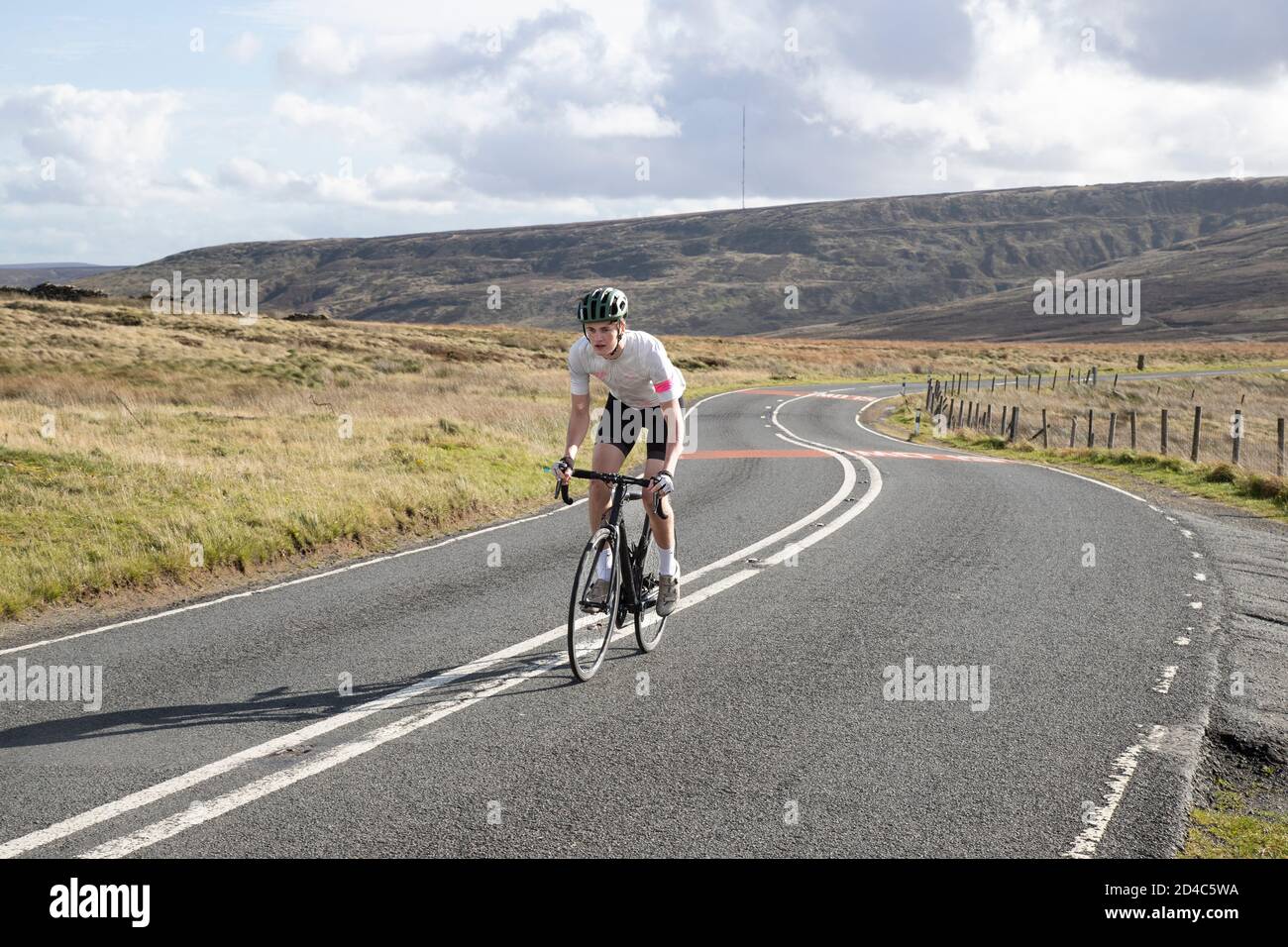 Giovane ciclista dalla sella che cavalca intenzionalmente su un Pendenza su una strada Yorkshire Moors con Holme Moss in lo sfondo Foto Stock
