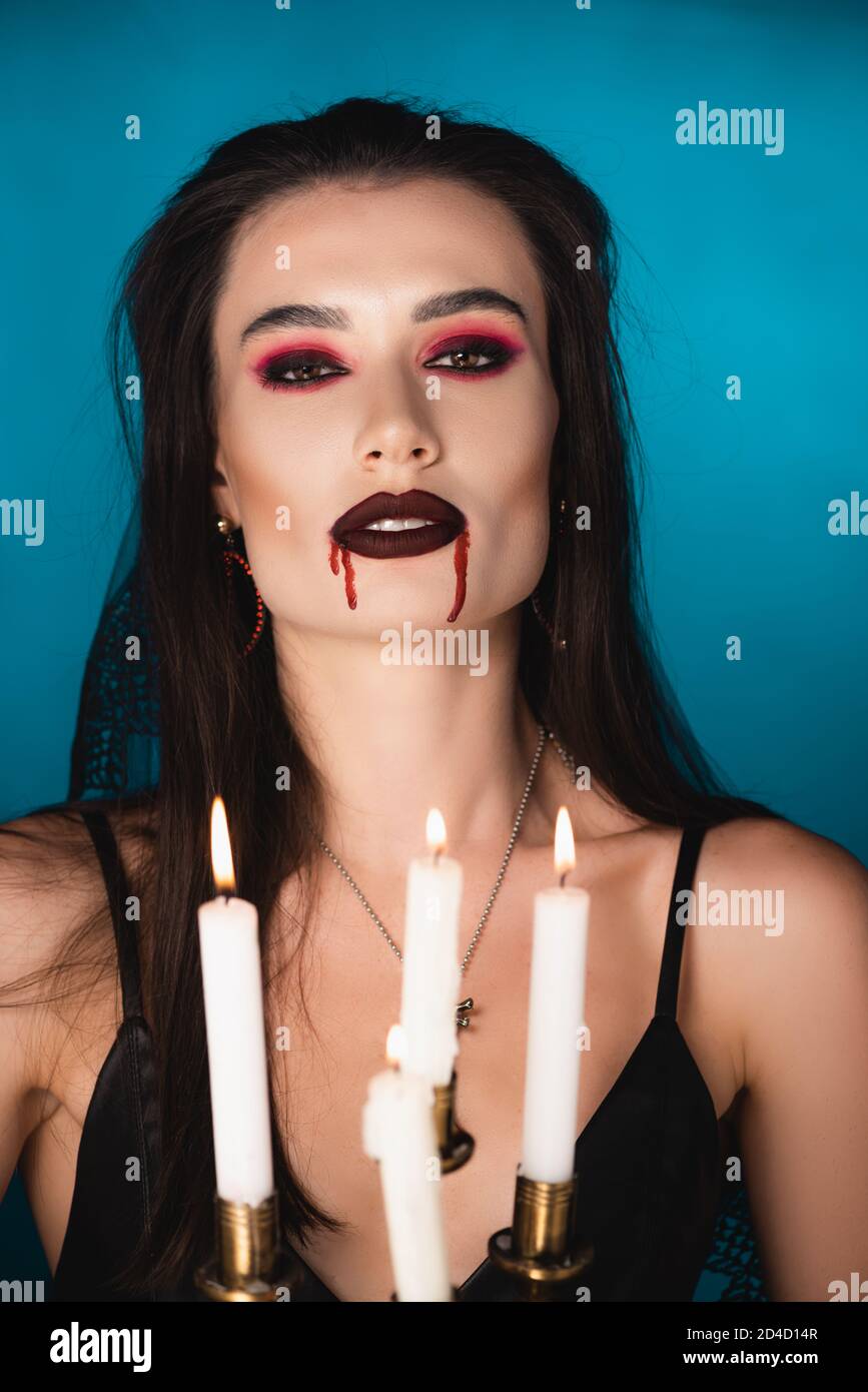 fuoco selettivo della donna con il sangue rosso sul viso vicino candele che bruciano su blu Foto Stock