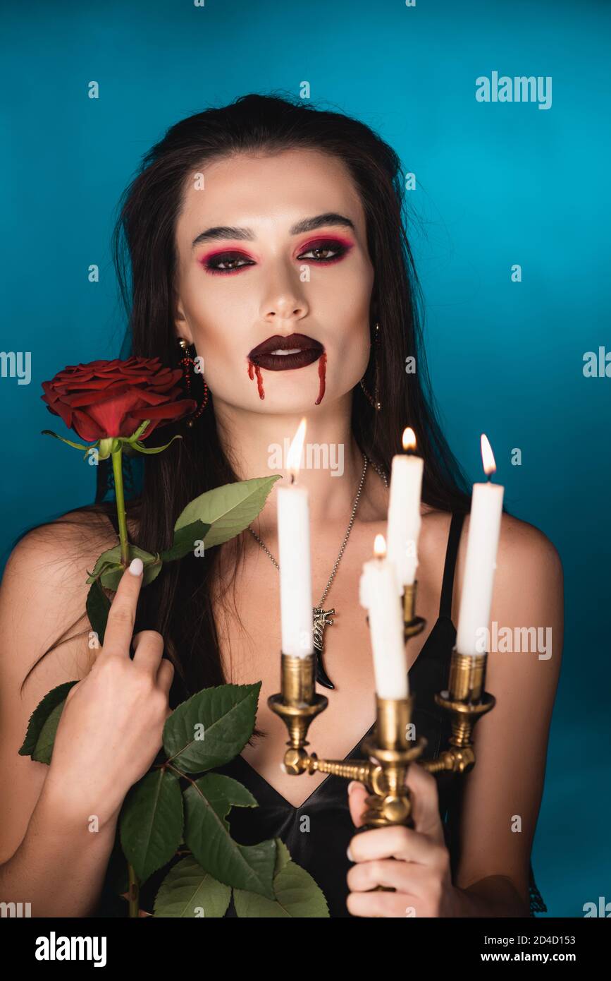 donna creepy con il sangue sulla faccia che tiene bruciando candele e. rosa rossa su blu Foto Stock