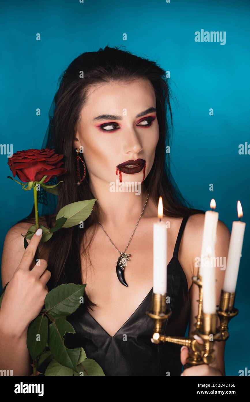 donna con sangue sul viso che tiene candele brucianti e rosso rosa su blu Foto Stock