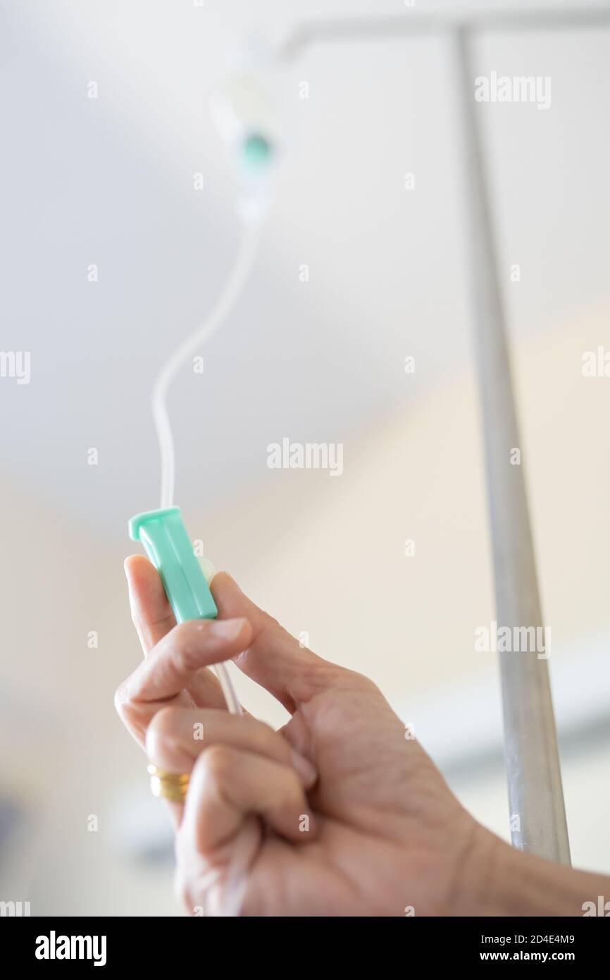 Consegnare l'infermiere della camera di gocciolamento IV che regola il flacone di infusione con paziente in ospedale Foto Stock