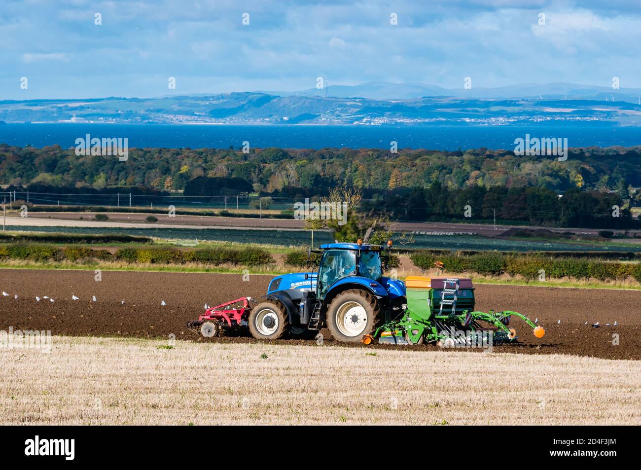 East Lothian, Scozia, Regno Unito, 9 ottobre 2020. Regno Unito Meteo: Un trattore agricolo che pianta un raccolto invernale con una vista del Firth of Forth Foto Stock