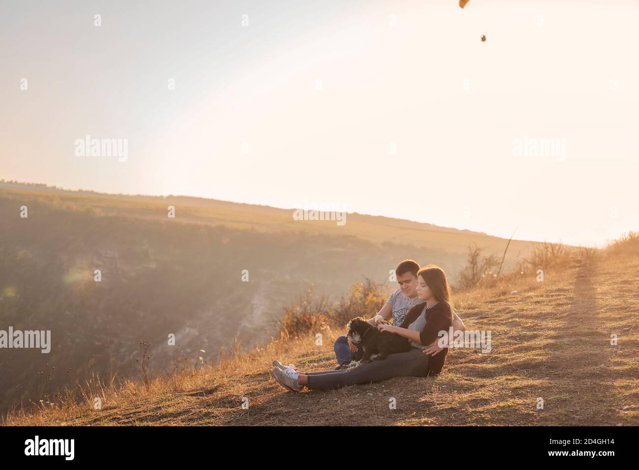 Seduto su un canyon, guarda i parapendio che volano nel cielo al tramonto. Viaggio con animali domestici. Giovane famiglia con un cane schnauzer viaggio. Moldavia, Vecchia Orhey Foto Stock