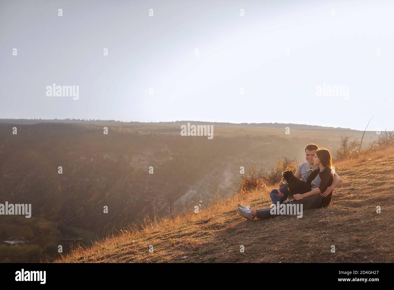 Seduto su un canyon, guarda i parapendio che volano nel cielo al tramonto. Viaggio con animali domestici. Giovane famiglia con un cane schnauzer viaggio. Moldavia, Vecchia Orhey Foto Stock