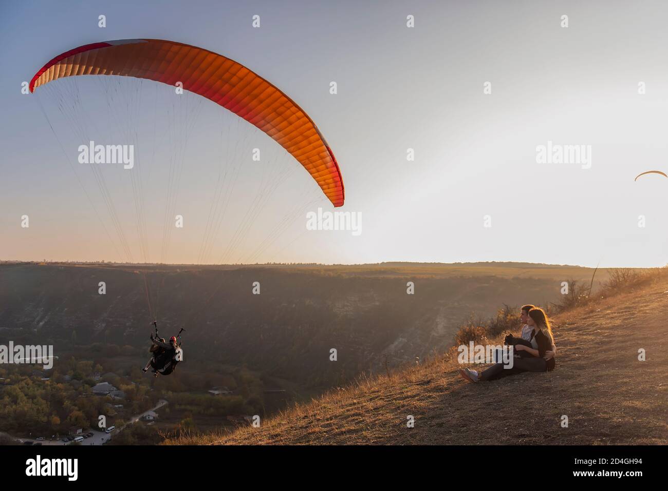 Seduto su un canyon, guarda i parapendio che volano nel cielo al tramonto. Viaggio con animali domestici. Giovane famiglia con un cane schnauzer viaggio. Moldavia, Vecchia Orhey Foto Stock