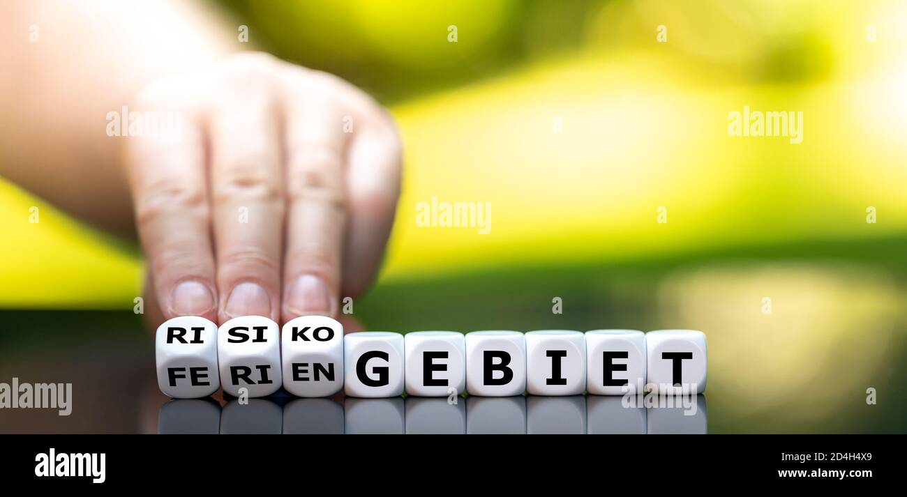 La mano gira i dadi e cambia la parola tedesca 'Feriengebiet' (destinazione di vacanza) in 'Risikogebiet' (area di rischio). Foto Stock
