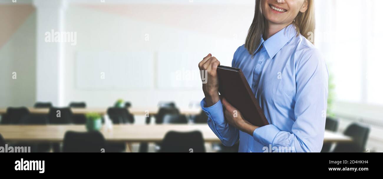 donna d'affari felice in blusa blu che tiene la tavoletta e in piedi su sfondo moderno dell'ufficio. spazio di copia della bandiera Foto Stock