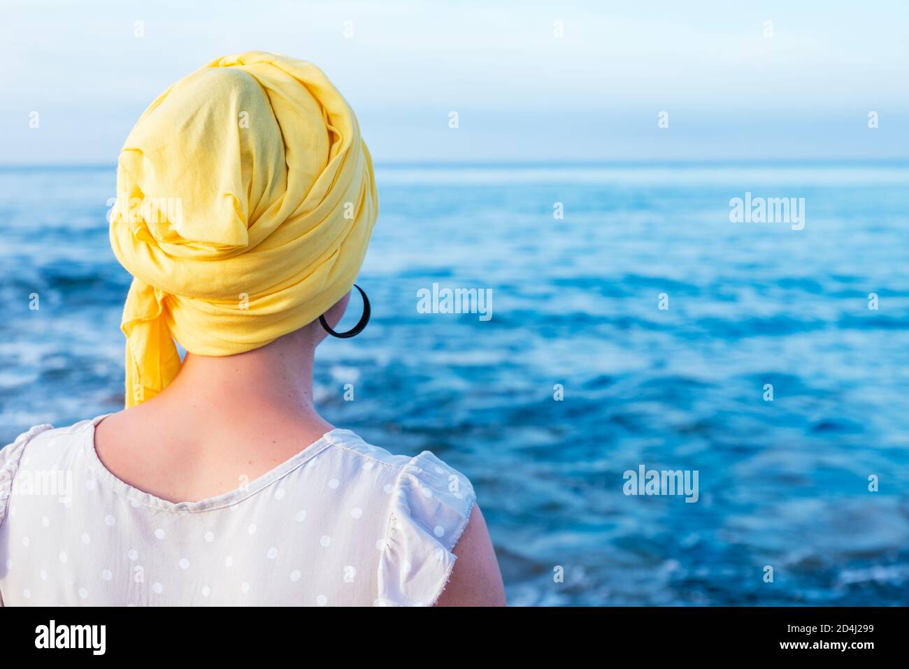 donna da dietro con sciarpa gialla che copre la testa senza capelli che  contemplano l'orizzonte del mare Foto stock - Alamy