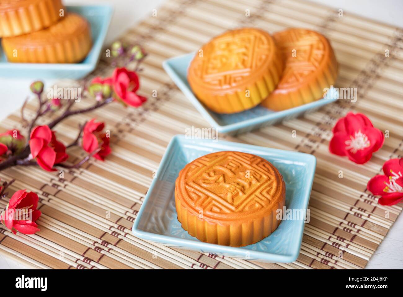 Composizione del festival cinese di metà autunno: Tradizionali torte cinesi sulla luna su piatti quadrati di ceramica blu circondati da rami con fiori rossi sono su una Foto Stock