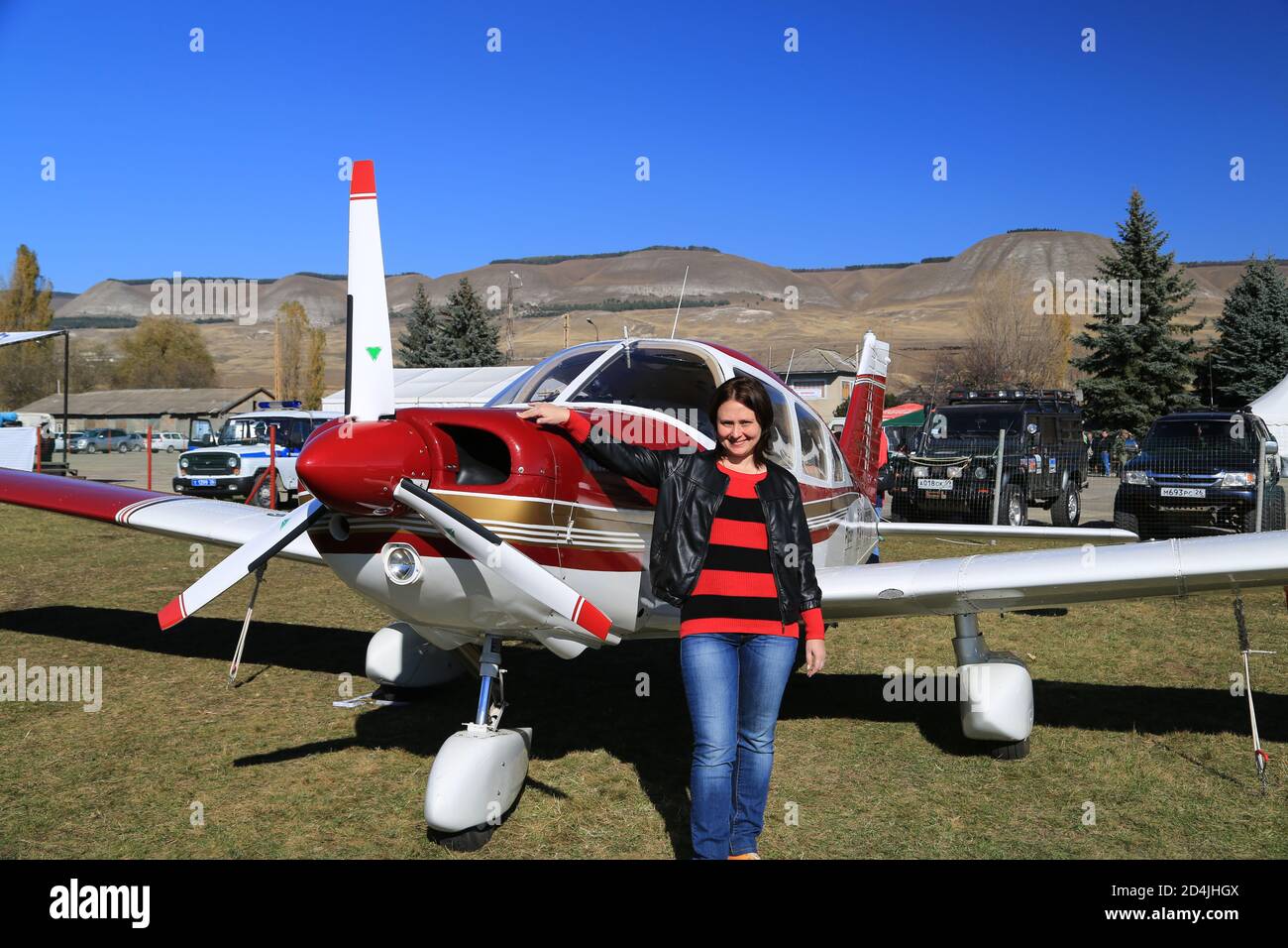 Una giovane donna si trova accanto ad un aereo ad uno spettacolo aereo con un sorriso. Foto Stock