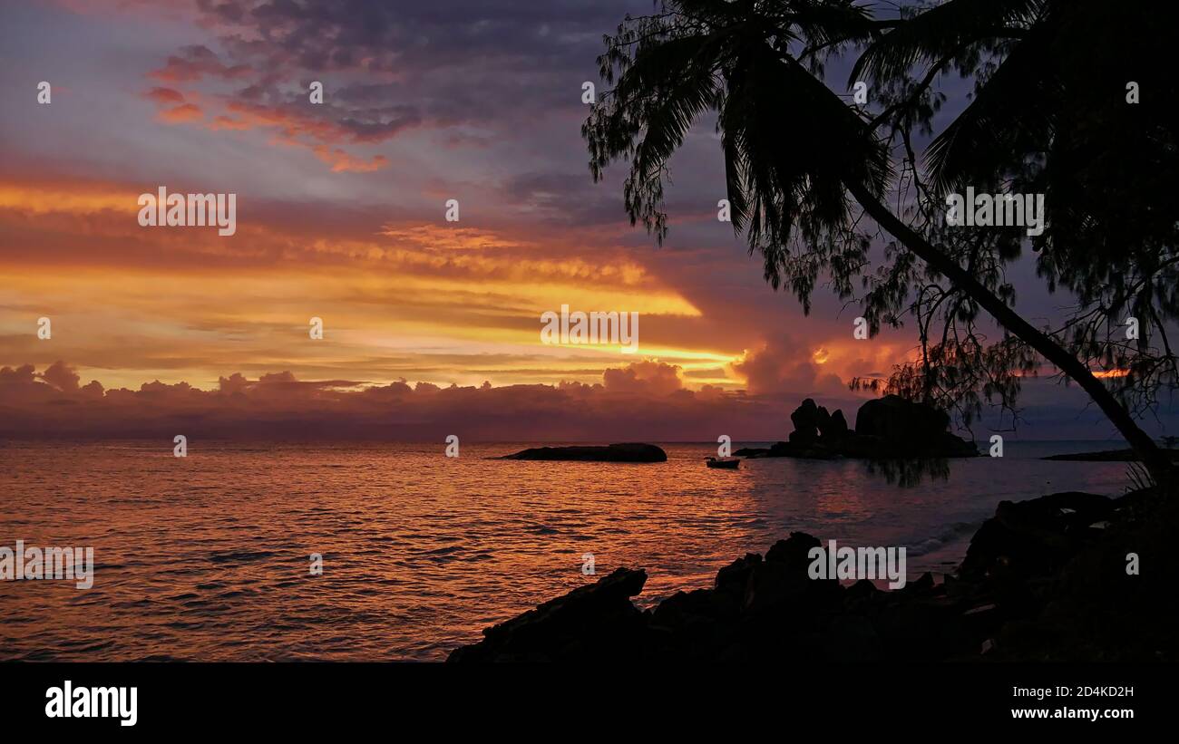 Splendido tramonto sulla spiaggia con cielo e fascio di sole color arancio, formazioni rocciose in granito nell'oceano e una barca a remi sulla costa di Praslin. Foto Stock