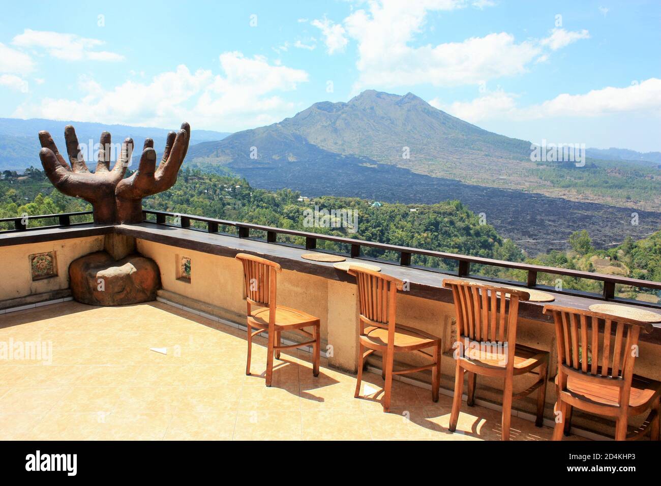 Kintamani, Bali / Indonesia - 3 settembre 2019: Vista del Monte Batur da una terrazza con una grande scultura a mani aperte e una fila di sedie in legno Foto Stock