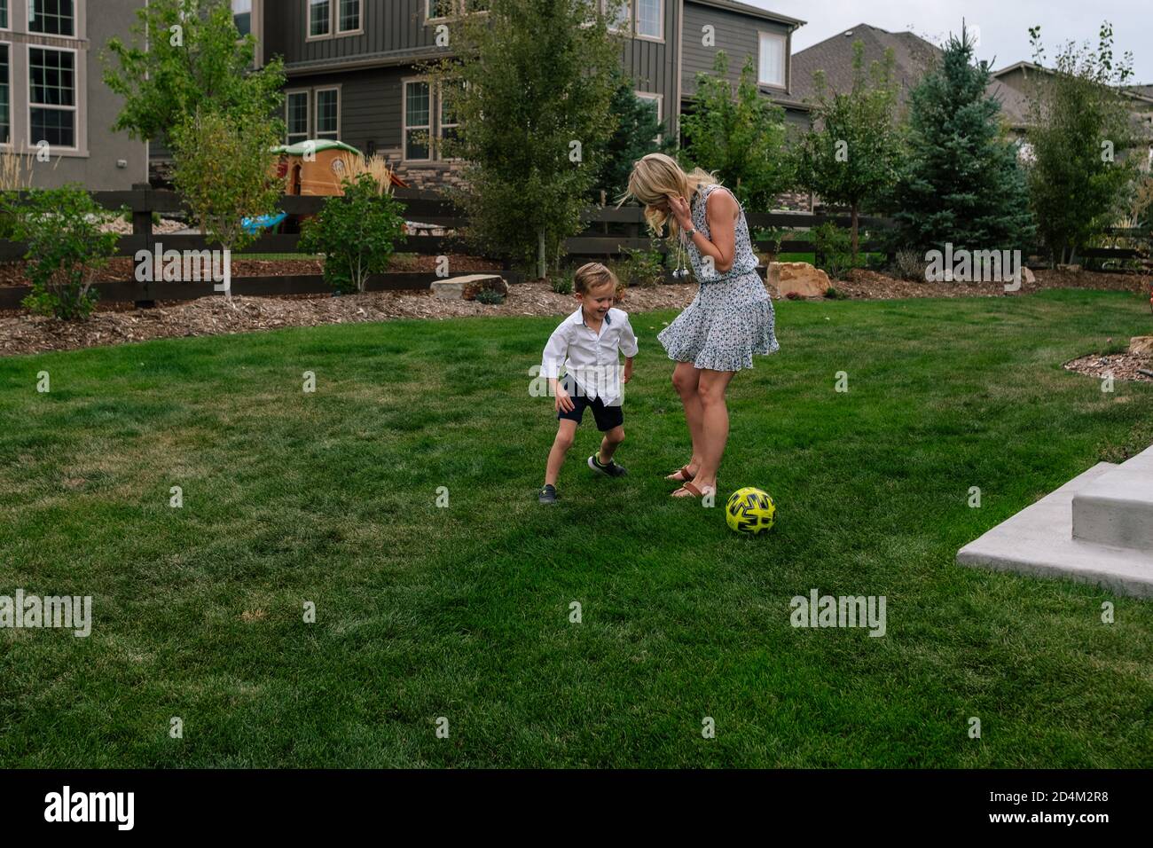 Ragazzino che gioca a calcio con la mamma in cortile Foto Stock